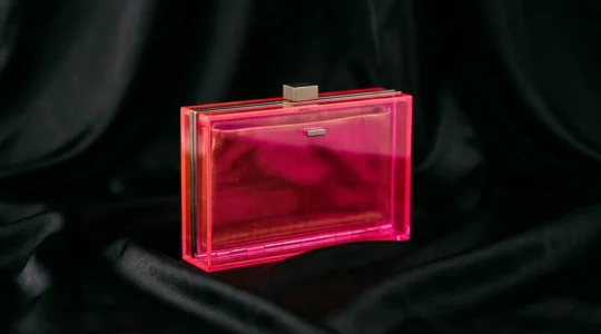Elegant neon pink clutch held beside a classic little black dress in sophisticated evening setting